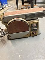 Front view of the belt and disc sander showing the circular sanding disc, sanding belt and control panel with label and on/off switch.