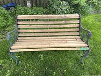 Front view of the wooden slat bench with cast iron decorative frame, showing slatted seat and backrest with metal fasteners.