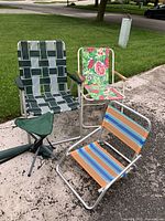 Overview of three outdoor seating items including two lawnchairs and one camping stool on pavement and lawn background.