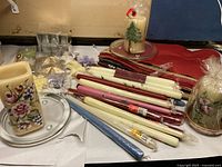 Lot showing various tapered candles, wax sheets, two glass plates, and pillar candles with packaging and some loose.