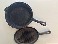 Top view of two cast iron pans on a light surface, one round skillet and one oval grill pan with ridges.