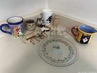 Overview of all cat-themed items including mugs, creamer, plate, figurines, and decor items arranged on countertop.