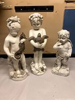 Front view of three cherub statues on table against wall, showing size and details