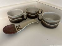 Three ceramic soup bowls with handles and a ceramic spoon rest, all placed on a white surface.