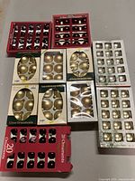 Multiple boxes of Christmas ball ornaments in different colors and sizes including red, black, gold, silver on a table.