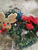 Close view of wooden reindeer door decoration, green wreath with red bows, and tangled multi-colored LED string lights on floor.