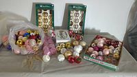 View of multiple assorted Christmas balls and ornaments including boxed and loose ones in a tote bag and a box.