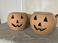 Two clay Halloween jack-o-lantern planters side by side, showing front view with carved faces and wide openings.