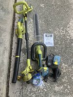 Full lot layout showing cordless whipper snipper, leaf blower, hedge trimmer, two batteries, charger, and trimmer line spools on concrete ground.