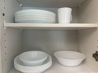 16 white plates and 1 white mug on the top shelf; 7 large bowls with 3 small plates and 2 small bowls on the bottom shelf