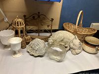 Overview photo showing all lot items including wicker basket at back, paintable cat, glass piggy bank, white vases, retro pot, and wicker decorative pieces.