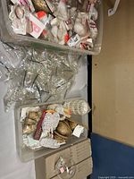 Top view of large tote filled with multiple new-in-bag ornamental birds, glass balls, and various small crafting supplies including mesh and gold ornamental cones.