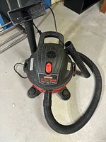 Top and side view of the Craftsman shop vacuum showing the main body, hose, and caster wheels on a concrete floor.