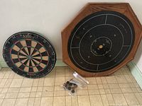 Photo of the crokinole board with playing discs bagged and the dartboard resting beside it.
