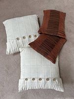 Set of four pillows on carpet showing contrast between off white square pillows with buttons and rust rectangular pillows with stripes.