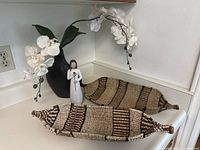 Black vase with white artificial orchids, two woven baskets nearby, and Willow Tree figurine on a white countertop corner