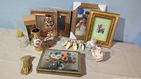 Photo of various home decor items including multiple photo frames, ceramic figurine, floral-themed artwork on metal box, and shell hanging decoration.