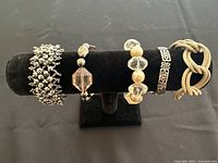 Five fashion bracelets displayed on a black velvet stand, showing varied bead styles and colors.