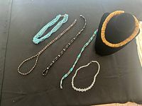 Full set of six fashion necklaces laid out on black surface showing variety in style and materials including wooden and magnetic beads.