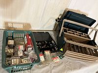 Wide shot of green plastic basket, small boxes of hardware, and large plastic tackle box on floor with contents partially visible