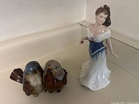 Two ceramic figurines shown: a pair of love birds and a lady in an elegant dress.