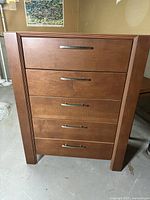 Front view of the five drawer dresser showing the wood finish and metal handles.