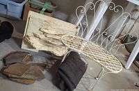 Photo of white iron bench, layered garden fountain, rolled-up screen, and flagstone pieces on basement floor.