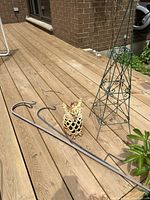Photo shows three metal garden hooks, small cast iron owl lantern, and small green metal trellis on wooden deck.