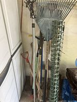 Photo of garden tools standing together including extended reach clippers, leaf rake, edger, shovels, axe, cultivator, and other tools.