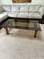 Full view of the coffee table showing the smoked glass top and wooden base in a living room setting next to a sectional sofa.
