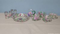 Photo showing entire set including 2 pairs of salt and pepper shakers, large glass bowl, 4 small footed bowls, and a small pitcher, all hand painted with floral designs.