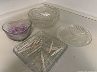 View showing pinwheel crystal salad bowl, two glass pickle trays, heart-shaped glass dish with pink stones, and several appetizer forks arranged on a kitchen counter corner.