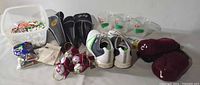 Bucket with assorted golf tees, a pack of Champ Fly golf tees, golf shoes, hand-painted golf ball ornaments, black John Baily golf club head covers, fuzzy maroon iron covers, and three clear plastic 19th hole drink cups.