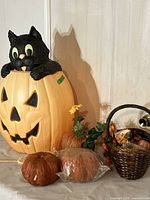 Full view showing large blow mold pumpkin with black cat and three artificial pumpkins alongside basket of Halloween decorations