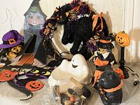 Wide view showing multiple Halloween decorations arranged on a surface including a wooden witch, a decorated wreath with black cat, ghost and pumpkin figures.