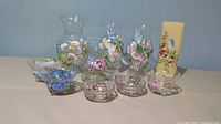 Lot of 8 hand painted glassware and decor pieces with floral designs including vases, bowls, and candle holder.