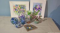 Full lot photo showing 4 hand painted glass vases, 2 round votive holders, 2 matted floral art prints, a flagstone welcome piece, and glass bonsai tree.