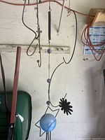 Two metal garden hooks hanging against a wall with wire and some green gardening equipment below.
