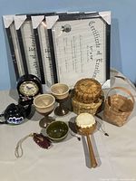 Four new black 11x14 photo/document frames sealed in plastic, stacked vertically with visible Certificate of Excellence prints. Surrounding items: small ceramic teapot, two ceramic wine glasses, small battery-operated clock, three small wicker baskets, a green fingertip bowl, and wooden monkey drum.