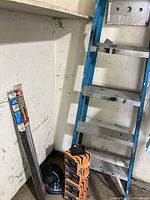 Photo of a 6-foot aluminum step ladder, foam sealer tube for garage doors, and four orange boxes of Tiger Claw hidden deck fasteners with installation tool on top.