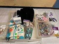 Overview of assorted jewelry making supplies in plastic containers with beads, stretch cords, and black display boards