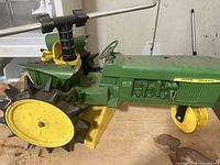 Side and front view of John Deere 4010 Diesel green model with yellow wheels and metal sprinkler attachment on top.
