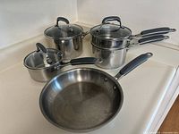 Full set of Kitchen Aid stainless steel pots and pans on a countertop showing 3-quart saucepan, double boiler, frying pan, and sauce pot