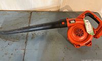 Side view of orange and black Black & Decker leaf blower with attached nozzle on metal surface
