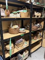 Two large black metal framed shelving units with pressboard shelves filled with various decorative baskets and ceramic items, contents included only for display and not part of the lot.