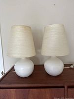 Pair of white ceramic globe table lamps on wood surface side by side