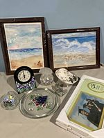 Two framed 11x14 original beach scene watercolor paintings, assorted decorative and kitchen items including floral-themed glass plate, covered dip bowl, perfume bottle, salt and pepper shakers, ceramic bathtub decor, floral clock, and new picture frames stacked.