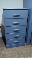 Front view of the blue painted chest of drawers showing five drawers with rectangular handles.