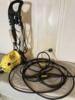 Full view of the yellow Karcher 205 pressure washer with attached hose and spray gun, showing the metal and plastic frame with brush attachments.