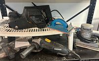 Photo showing Black & Decker belt sander along with blue hand sander, Mastercraft angle grinder and Craftsman rotary tool on a shelf and bench.